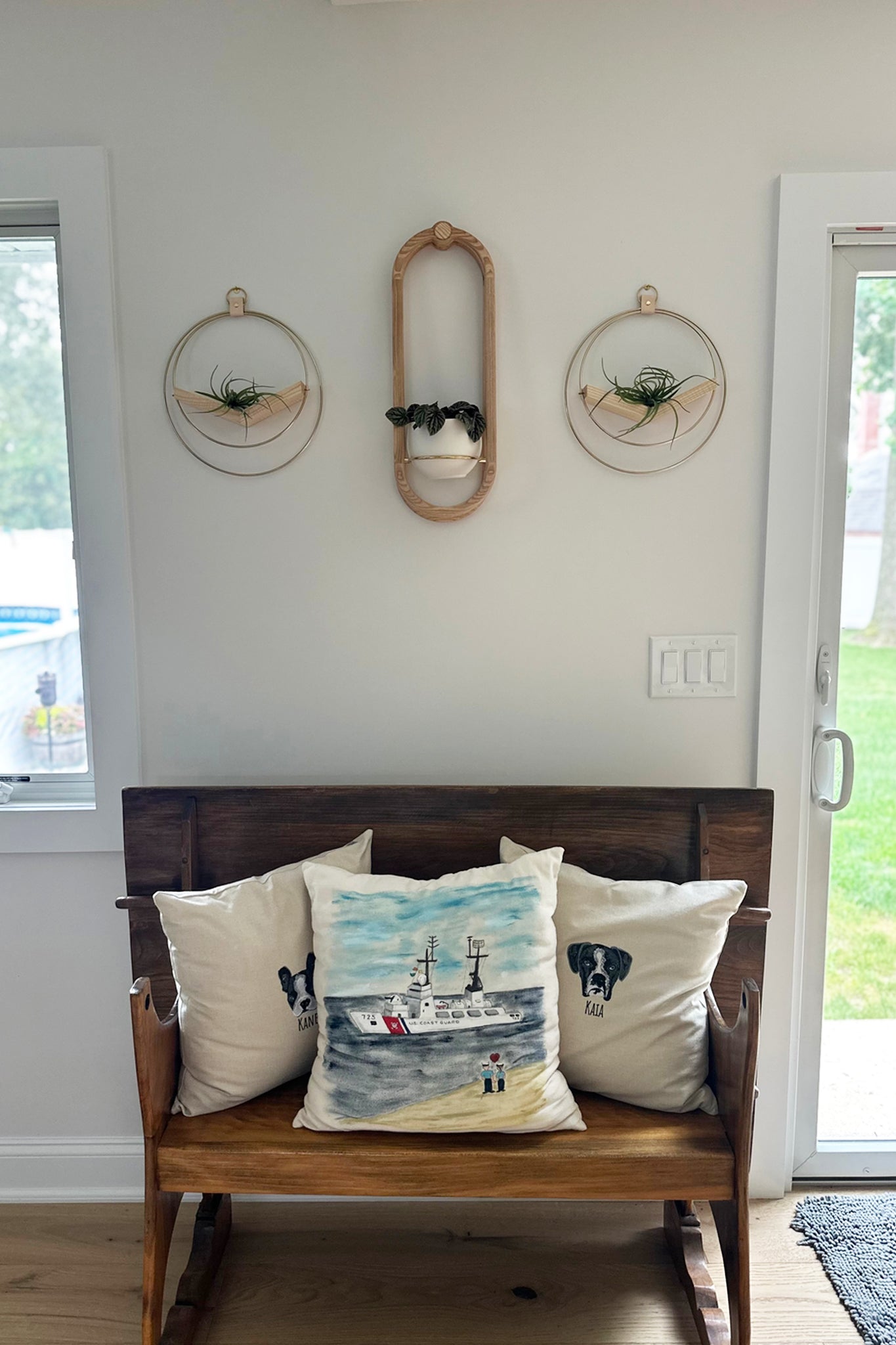 Wooden bench with decorative pillows against a white wall with the Frame Wall Planter and V-Hanger mix on the wall.