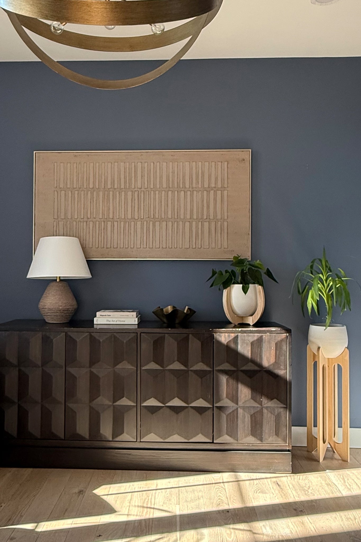 Modern interior with a dark wooden sideboard, decorative lamp, and the Nested & Arches Plant stands against a blue wall.