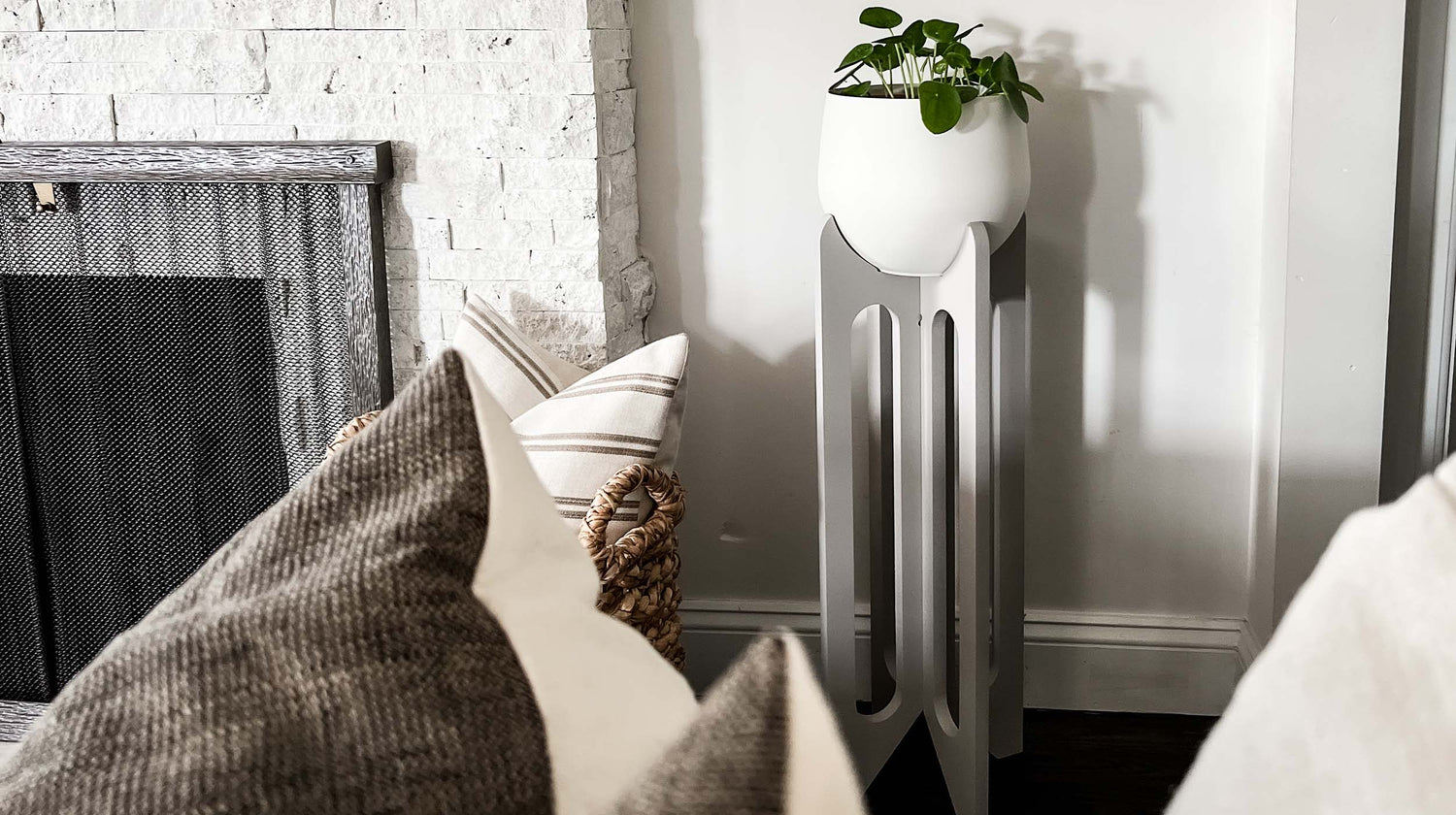 braid & wood tall plant stand in gray with white pot and houseplant next to fireplace