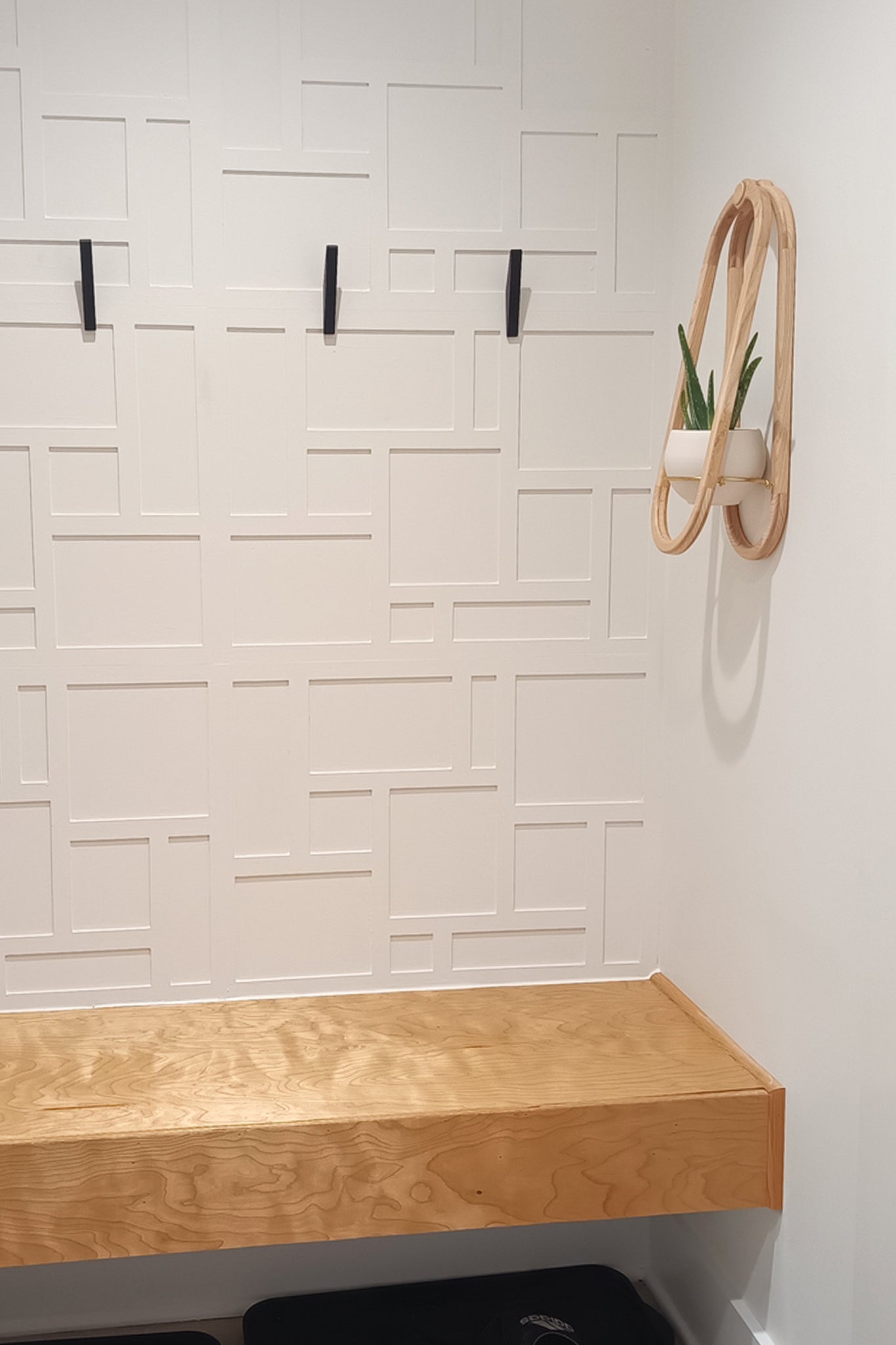 Wooden wall-mounted shelf against a textured white wall with a plant aove a wood bench