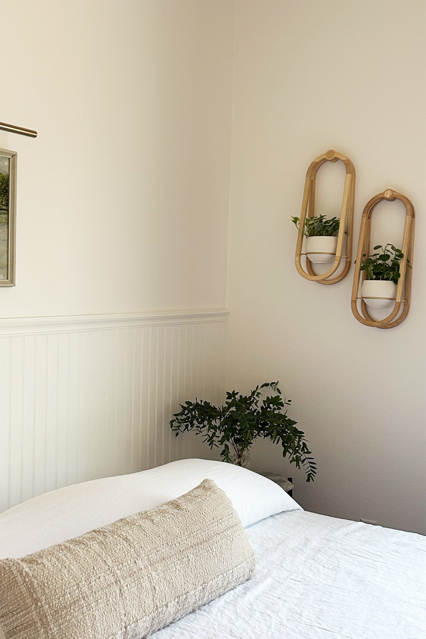 A simple bedroom with light linen bedspread, framed artwork, and two Frame Wall Planters on the wall with houseplants.