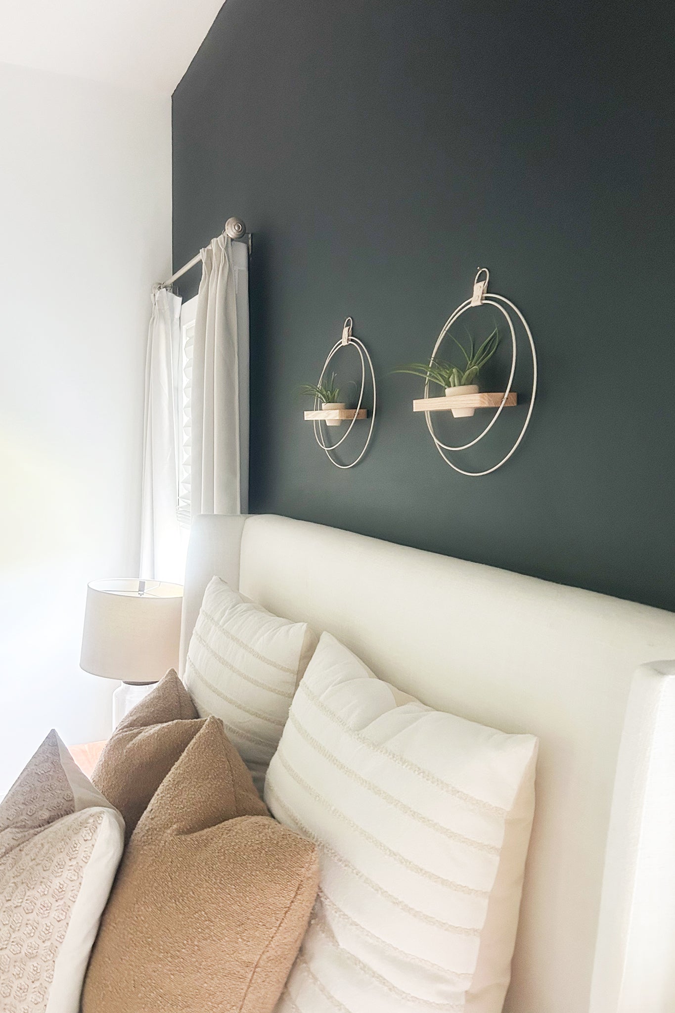 side view of two modern plant shelves made of white ash wood with light metal rings and blush terracotta pots above a bed