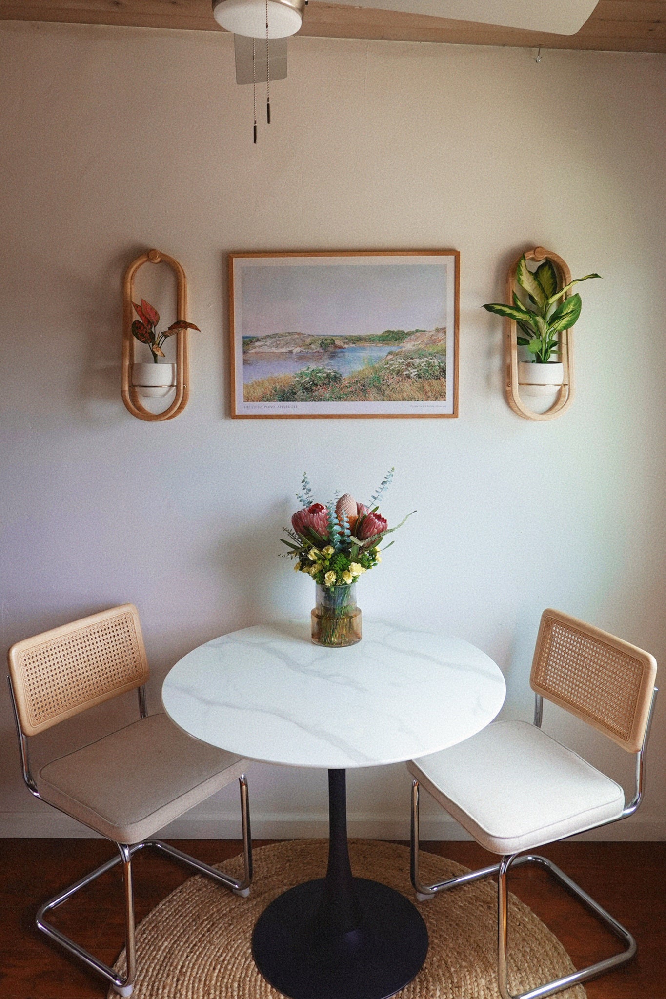Small dining area with a round table and two chairs, featuring wall art and the Frame Wall Planter Duo.