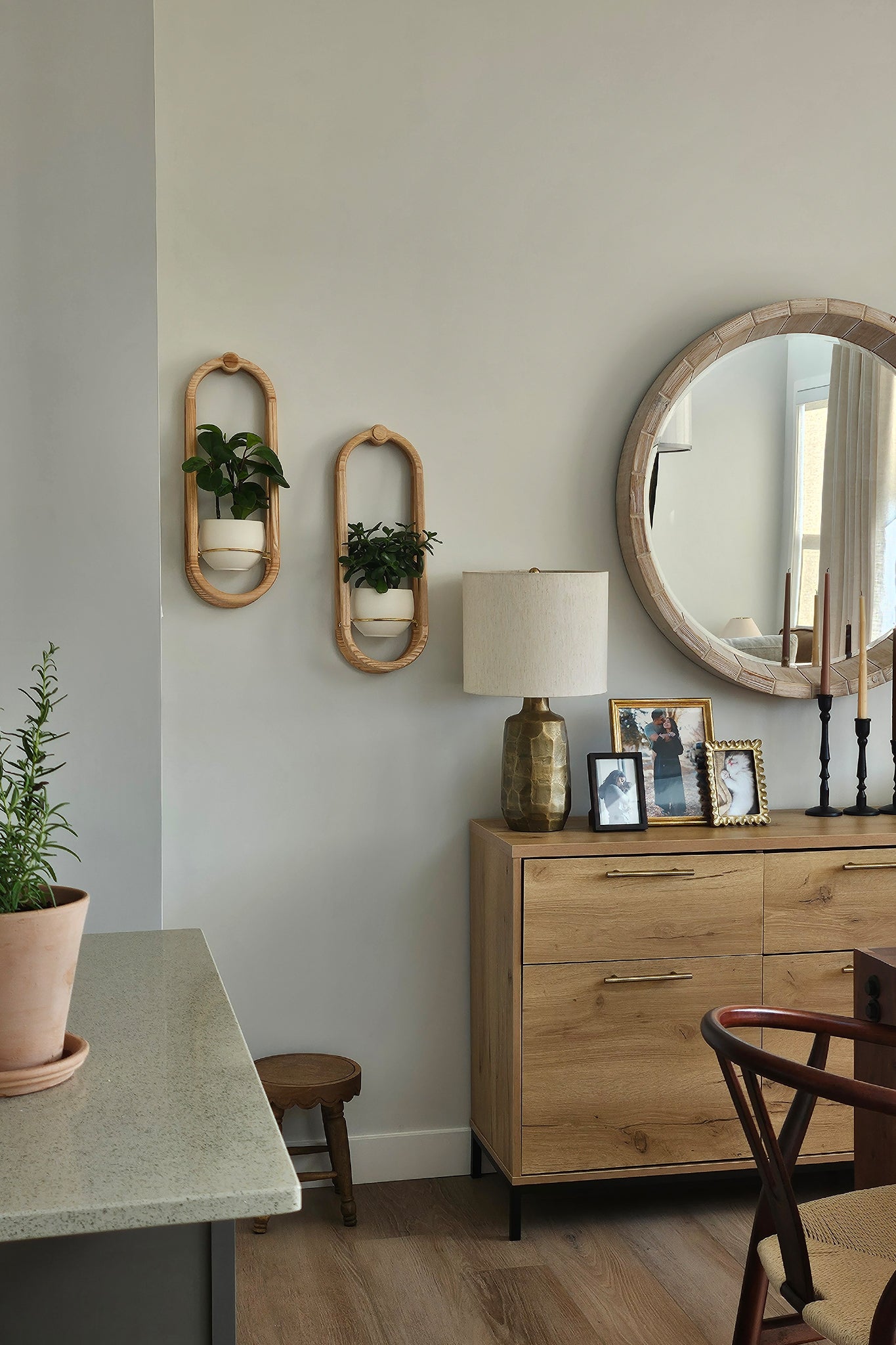 A modern dining room with a wooden console table, round mirror, scandi dining charis, and two Frame Wall Planters on the wall.