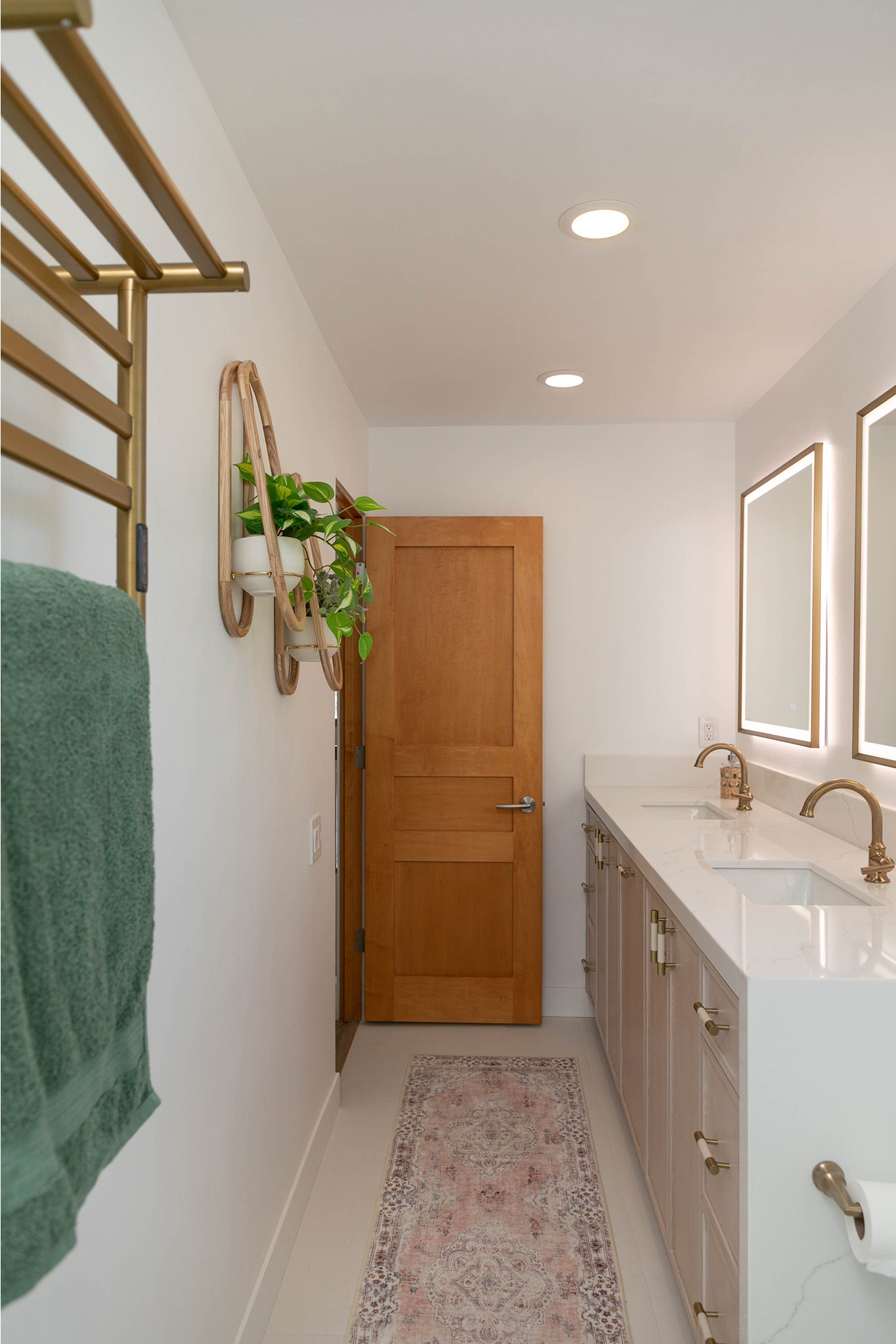 A clean and modern bathroom with white countertops, a pink rug, a green towel, and two Frame Wall Planters on the wall.