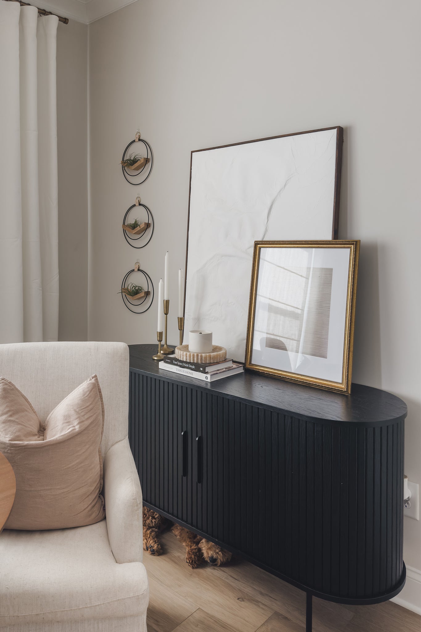 Modern living room with a black console table, beige armchair, wall art, and three wall-mounted circular air plant hangers in a vertical line on the wall.