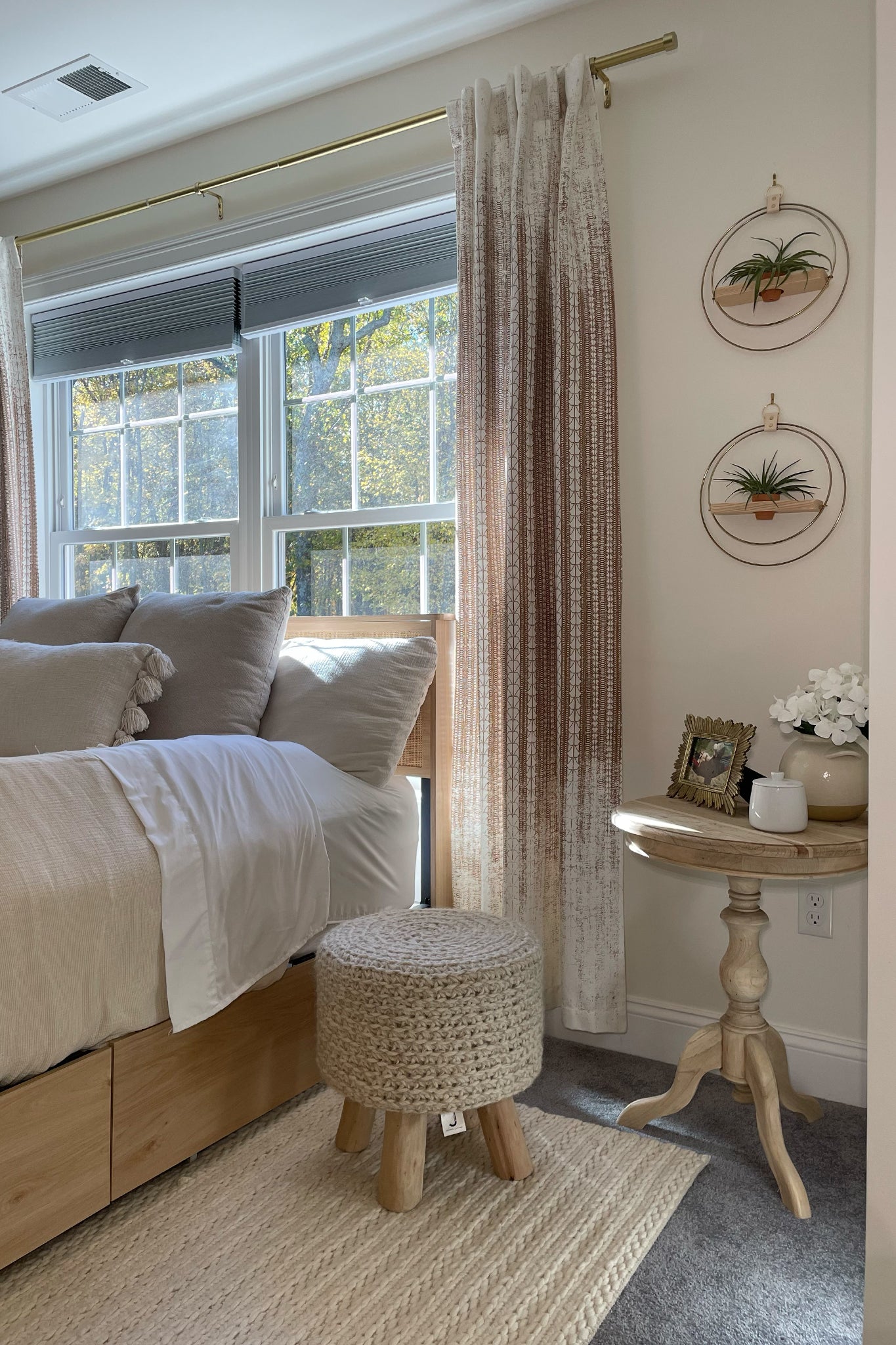 Cozy bedroom with wooden bed, ottoman, and side table with two wall-mounted circular planters with air plants in a terra cotta pot on the wall next to the window.