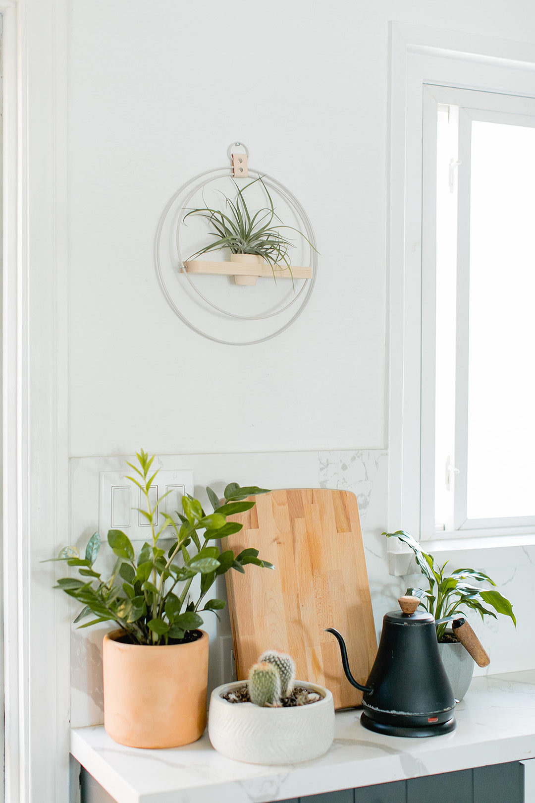 braid and wood plant shelf styled on wall above cutting board and electric kettle