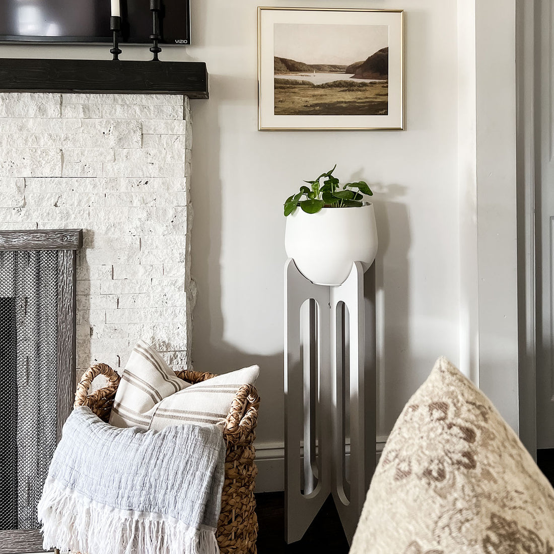 tall gray plant stand and white pot by braid & wood styled next to fireplace in modern living room