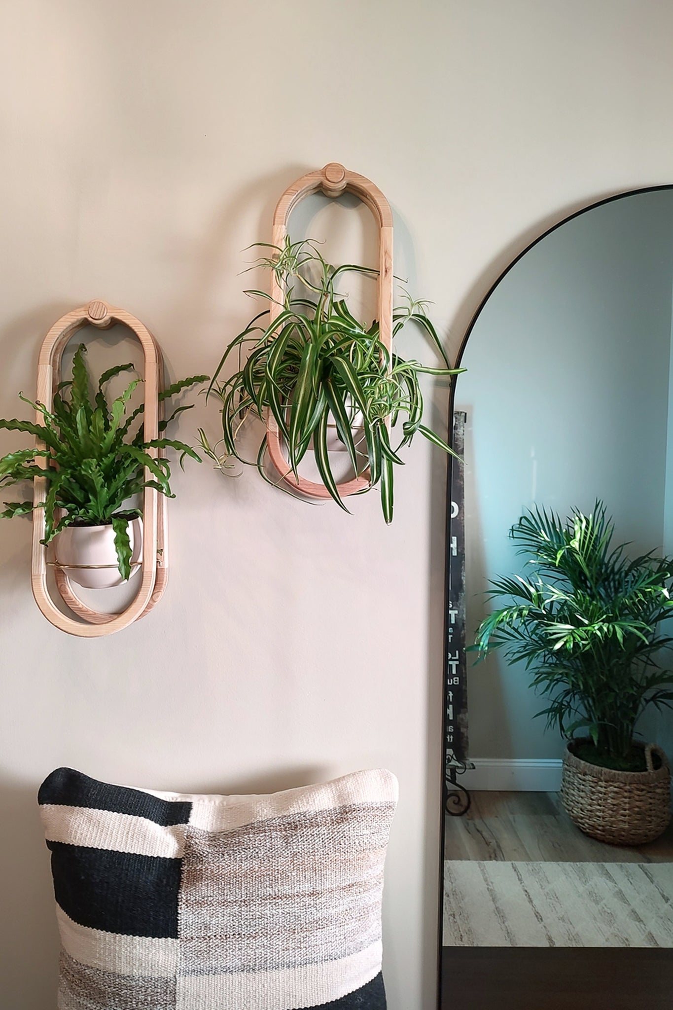 Two wall-mounted Frame Wall Planters with plants on a light-colored wall, next to a mirror reflecting a plant.