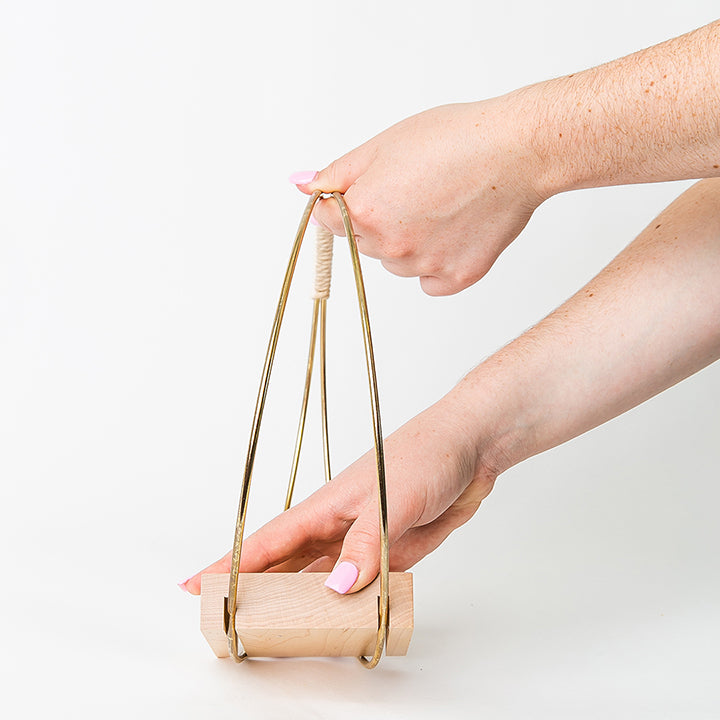 person assembling gold plant hanger by braid & wood