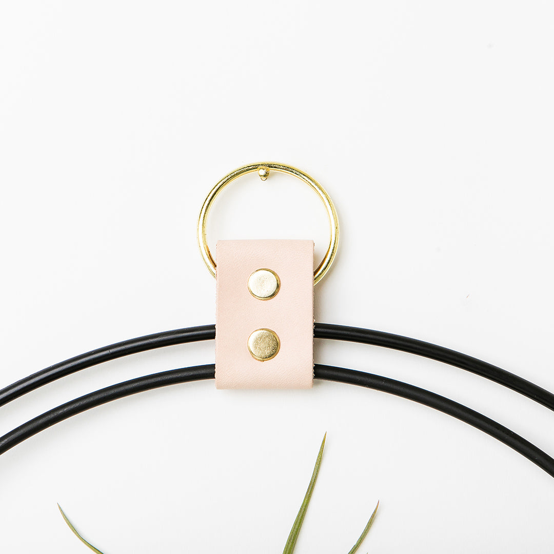 up close view of leather detail on black and gold metal plant shelf with maple base