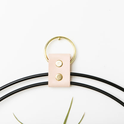 leather strap detail of plant shelf with black and gold metal and maple wood base with black pot