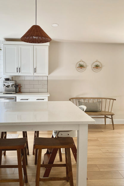 A modern kitchen with white island, wooden stools, and two wall-mounted circular planters with air plants in a terra cotta pot above a bench.