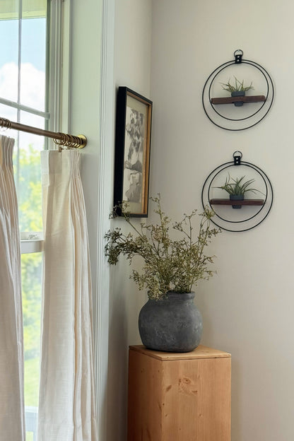 A detail shot of a dining room corner with a window, framed picture, wooden cabinet, and two wall-mounted circular planters with air plants in a terra cotta pot on a neutral wall.